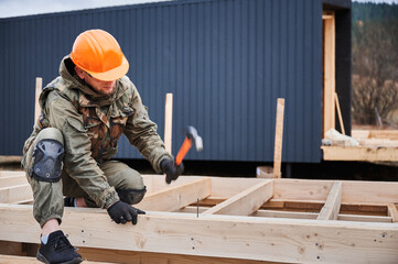 Man worker building wooden frame house. Carpenter hammering nail into wooden board, using hammer....