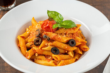 Penne pasta in tomato sauce, tomatoes decorated with parsley on a wooden background