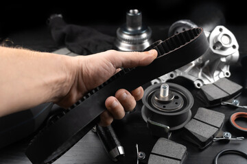 Fototapeta na wymiar Timing belt and tension rollers of gas distribution system of car engine, concept of car maintenance. Master's hand holds timing belt against background of spare parts.