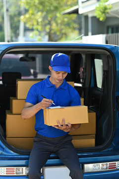 Delivery man in blue uniform using digital tablet while standing at open van full of delivering package