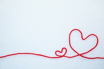 柔らかそうな白背景に一本の赤い糸で作られたシンプルな大小二つのハートの形の可愛いメッセージフレーム