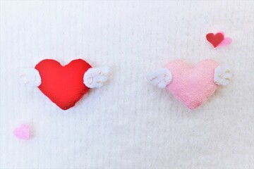 柔らかい布地の白バックにフェルトで出来た赤とピンク色の２つの羽つきハートの形
