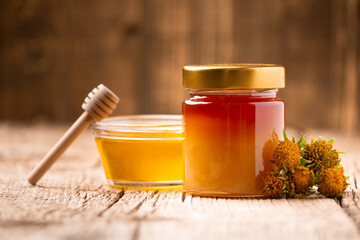 Honey in a glass jar and flowers on a wooden background