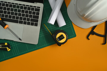 Laptop computer, blueprints, safety hardhat, coffee cup and stationery on yellow background