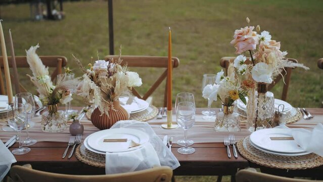 Close-up table served and decorated with candles and dried and pastel flowers for boho style wedding dinner, plates and wne glasses, no people shot, slow motion.