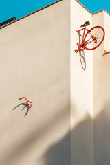 The rear half of a vintage bicycle and a red handlebar pinned to the wall of a minimalist building block with a turquoise blue sky