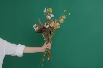 Florist makes a bouquet of dried flowers at a wooden table on a plain dark background with copyspace