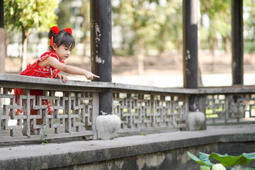 Happy asian little girl in Chinese traditional costume pointing to lotus in a pond.