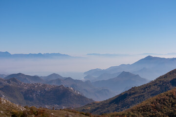 Panoramic view of dramatic karst mountain chains Dinaric Alps surrounding the Lake Skadar National Park seen from Goli Vrh, Montenegro, Balkan, Europe. Valley is covered by mystical fog, blue hills