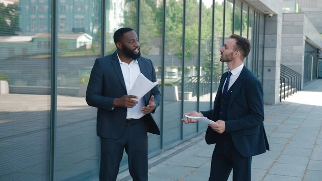 Two satisfied male entrepreneurs rejoice at successful win-win deal and discuss further cooperation. Business colleagues giving high five to each other while standing in business district
