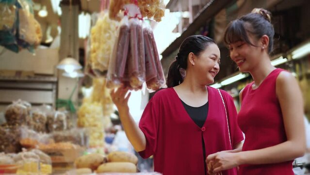 4K Happy Asian family mother and daughter choosing and buying raw food and groceries for cooking celebrating Chinese Lunar New Year festive at Bangkok Chinatown street market. Chinese culture concept.