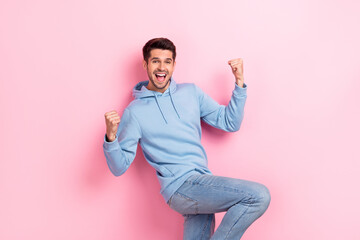 Photo of good mood lucky guy dressed blue sweatshirt rising fists shouting yelling isolated pink...