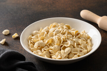 Healthy homemade dry orecchiette pasta in bowl on brown tabletop. Close up.