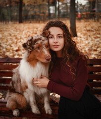 Кed head girl with dog sitting on bench in autumn park 