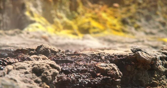 Mineral liquid flowing on rocks with yellow sulfur in background, focus pull