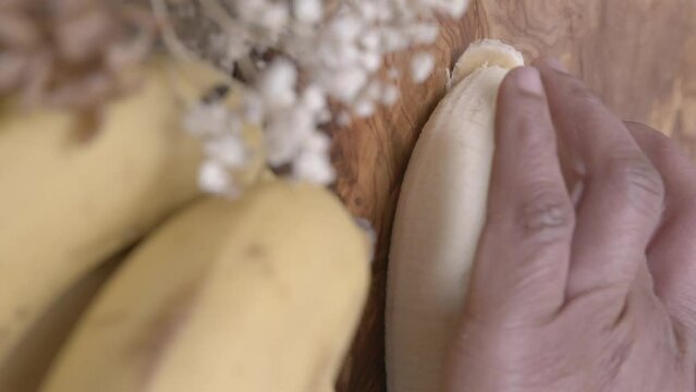Metal kitchen knife cutting a banana into thin slices on a cutting board.
