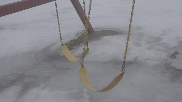 A yellow swing swaying back and forth in the fog during winter.