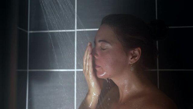 Woman showering face and body relaxing in shower bath. Person washing face
