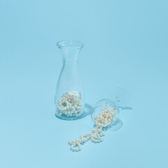 Glassware with pearls, creative aesthetic layout against pastel blue background. Sparkling refreshment idea, soft summer light. 