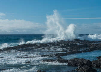 Big waves splash against black lava rock in the Atlantic Ocean near Los Gigantes, Tenerife, Canary islands, Spain. Sunny winter day.