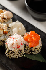 Sushi on black plate served with soy sauce, wasabi and ginger over grey background. Traditional Japanese food.