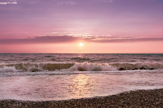 Sea splashing waves backlit by setting sun in front of beautiful sunset sky background. Toned image in trendy magenta color of year 2023. Nature background. Great wallpaper design. Copy space.