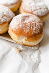 Krapfen, Berliner doughnuts or Pfannkuchen with powdered sugar filled with custard wrapped in white paper fresh from German bakery, traditional fried yeast dough pastry for New Year or carnival party - 556941560