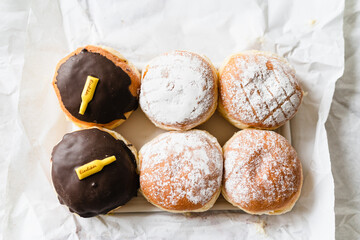 Assorted Krapfen, Berliner doughnuts or Pfannkuchen filled with jam or custard wrapped in white paper fresh from German bakery, traditional fried yeast dough pastry for New Years or carnival party - 556941564