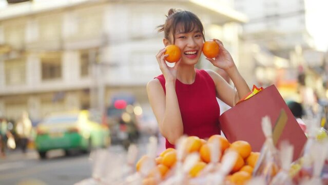Portrait of Attractive Asian woman holding shopping bag choosing and buying orange fruit at Bangkok Chinatown street market for celebrating Chinese lunar new year festival. Chinese culture concept.
