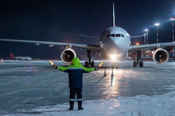 Airliner marshalling at the aiport apron at winter night. Passenger aircraft meeting