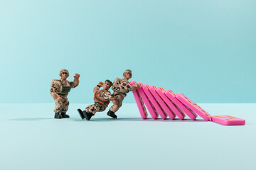 Toy soldiers stoping domino effect of pink domino on cyan background