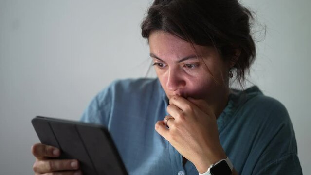 Anxious Woman staring at tablet with concerned emotion. Preoccupied expression of female person looking at screen browsing internet using technology