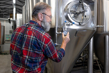 Fototapeta na wymiar Brewery worker controlling the pressure in tanks with beer