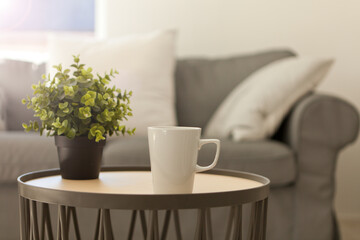 Fototapeta na wymiar cup of hot tea. white mug on table near cozy gray sofa. pillows and blanket. Home relax Lifestyle