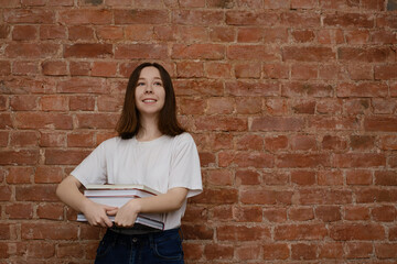 Girl in a white t-shirt with a stack of books. Brick background. Girl on the background of a brick wall.
