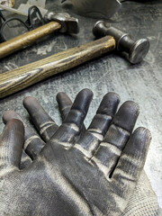 Black blacksmith work gloves against a sledgehammer background. Hard men's work as a blacksmith.
