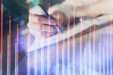 Financial forex graph displayed on hands taking notes background. Concept of research. Double exposure