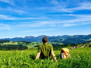 Bayern, Allgäu, Mann, Person beim Wandern macht Pause, Rast auf Wiese mit Aussicht auf Berge