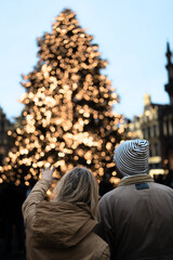 Couple look at the blurred christmas tree, girl pointing at the tree with her finger