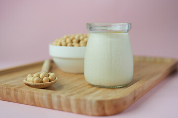 soy milk pouring in a glass jar on light pin background 