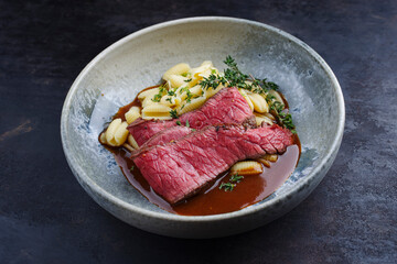 Fototapeta na wymiar Traditional Italian chianina sliced roast beef with gnocchetti sardi pasta in spicy red wine sauce served as close-up in a Nordic design bowl with copy space