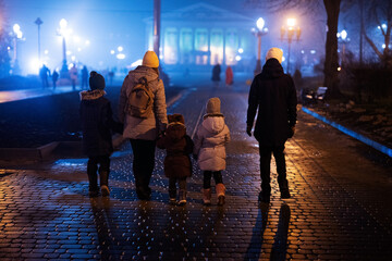 Back of family walking in night foggy city.