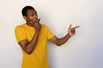 Portrait of uncertain young man pointing aside over white background. African American guy wearing...