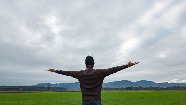 Man with spread arms standing under dramatic sky