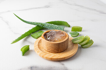 aloe vera gel in a wooden bowl on a marble background with leaves and slices of fresh aloe. the...