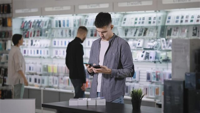 At the gadget store. A man chooses a new smartphone, compares design and features.