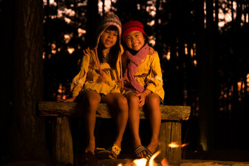 Fototapeta na wymiar Cute little sisters warm near campfire outdoors in cold weather. Children having fun at camp fire. Camping with children in winter pine forest. Happy family on vacation in nature.