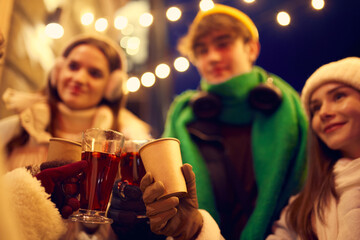 Happy young men and girls, friends walking at festive Christmas street and drinking mulled wine....