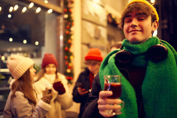 Emotional young people, friends meeting, smiling, drinking hot drinks at evening city street at winter time. Emotions, love, friendships, ad, sales concept