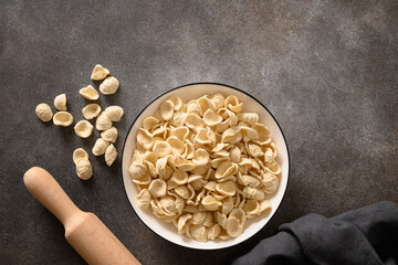 Raw apulian Orecchiette pasta made from whole wheat flour on dark tabletop. View from above.